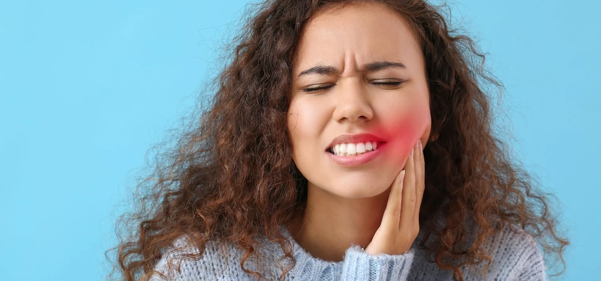 A woman holding her cheek while experiencing dental discomfort